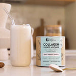 A creamy collagen powder drink with a straw sits next to a canister of Nutra Naturals Collagen Joints + Bones on a kitchen counter, emphasizing bone health support. A spoon lies nearby, with the softly blurred background adding warmth.
