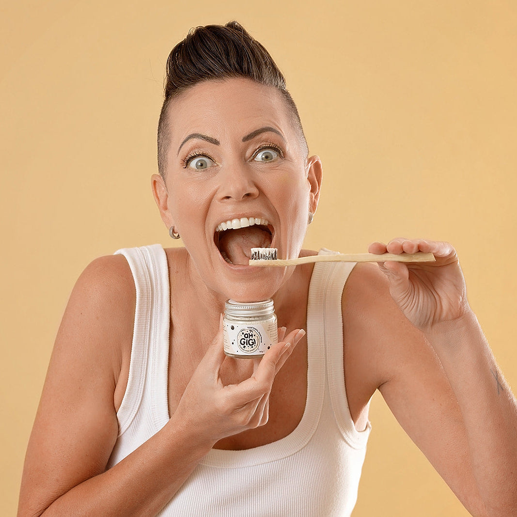 Woman holding Oh Gigi Flavour-Free Hydroxyapatite Tooth Powder and brushing her teeth