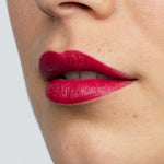 Close-up of smooth skin and full lips wearing Antipodes Moisture Boost Natural Lipstick in a vibrant, glossy plum shade. The text "Oriental Bay Plum" highlights its long-lasting color.
