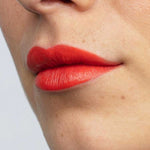 Close-up of lips wearing Antipodes Moisture Boost Natural Lipsticks 4g in Piha Beach Tangerine, a bright orange shade. Smooth skin with small moles is visible; lipstick is enriched with moisturising avocado oil.