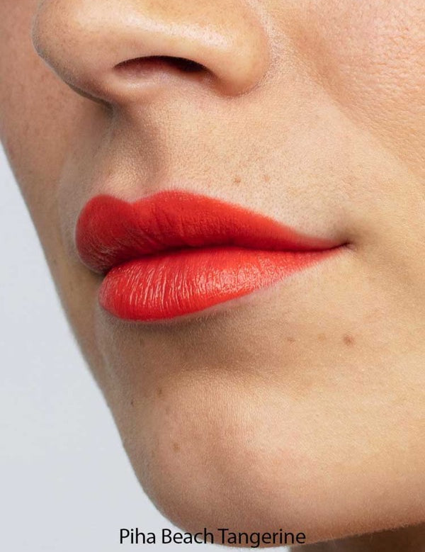 Close-up of lips wearing Antipodes Moisture Boost Natural Lipsticks 4g in Piha Beach Tangerine, a bright orange shade. Smooth skin with small moles is visible; lipstick is enriched with moisturising avocado oil.
