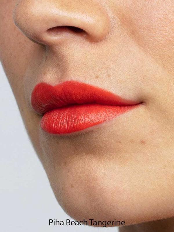Close-up of lips wearing Antipodes Moisture Boost Natural Lipsticks 4g in Piha Beach Tangerine, a bright orange shade. Smooth skin with small moles is visible; lipstick is enriched with moisturising avocado oil.