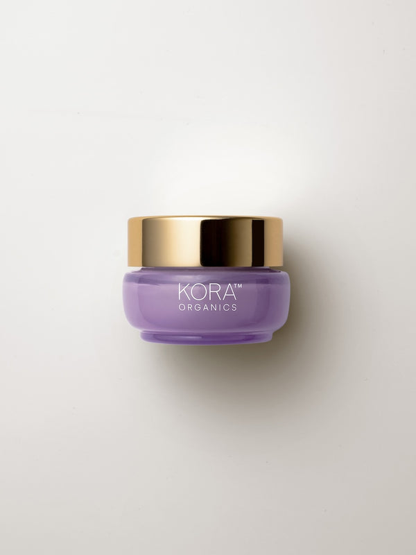 Small low purple 15 ml jar of KORA Plant Stem Cell Retinol Alternative Moisturiser with a wide gold lid, lying on a warm grey surface.