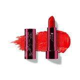 Hibiscus lipstick in vivid orange red, standing in a reflective pink tube beside its botanical patterned cap, with a matching bright red smear behind.