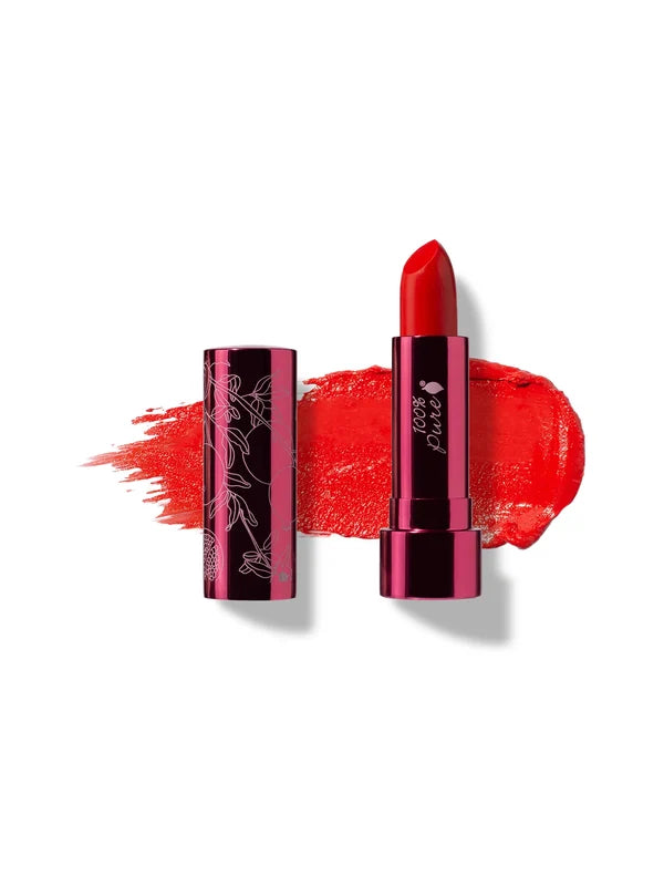 Hibiscus lipstick in vivid orange red, standing in a reflective pink tube beside its botanical patterned cap, with a matching bright red smear behind.