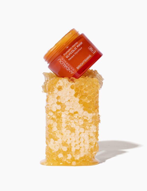 Andalou Naturals Brightening Pumpkin Honey Glycolic Mask jar resting on fresh honeycomb