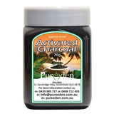 A jar labeled Pure Eden Activated Charcoal 150g sits before a tropical backdrop of palm trees and a waterfall. Made in Australia from coconut shell charcoal, the label includes contact details and an address.
