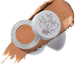 A small open container of 100% Pure Fruit Pigmented® Long Last Concealer with Super Fruits 3g in a golden peach shade rests on a matching smear. The white lid has a floral design, and the text Golden Peach appears below. Brand: 100% Pure.