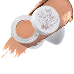 An open container of 100% Pure Fruit Pigmented® Long Last Concealer with Super Fruits 3g in Peach Bisque, featuring a floral lid design. A smear of this peachy-beige concealer by 100% Pure is displayed in the background.