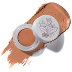 A jar of 100% Pure Fruit Pigmented® Long Last Concealer with Super Fruits 3g, featuring a botanical lid design, sits on a swipe of medium brown Toffee shade, offering vegan coverage from the brand 100% Pure.