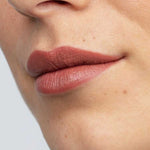 Close-up of smooth lips wearing Antipodes Moisture Boost Natural Lipsticks 4g in a matte mauve-brown shade. The natural formula provides long-lasting color. Text at the bottom reads: Queenstown Hot Chocolate.