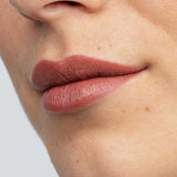 Close-up of smooth lips wearing Antipodes Moisture Boost Natural Lipsticks 4g in a matte mauve-brown shade. The natural formula provides long-lasting color. Text at the bottom reads: Queenstown Hot Chocolate.
