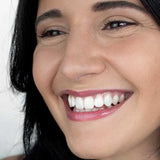 A person with dark hair smiles, showing bright teeth and wearing subtle, rosy lip balm. The text at the bottom reads: Hurraw! Organic Lip Balm - Raspberry 4.8g.