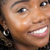 A woman with radiant skin and a bright smile wears a glossy pink lip color. Text at the bottom left reads: "Hurraw! Organic Lip Balm - Raspberry 4.8g—vegan & organic.