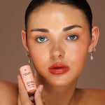 Model wearing Avocado Zinc SPF50 Natural Lip & Cheek Tint in Red Earth and holding the tint beside her face.