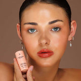 Model wearing Avocado Zinc SPF50 Natural Lip & Cheek Tint in Red Earth and holding the tint beside her face.