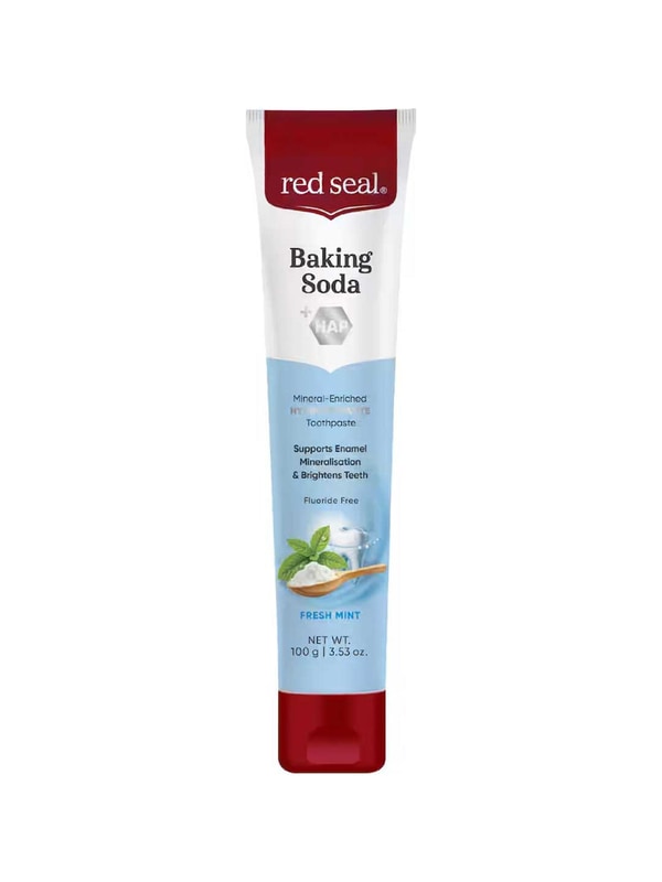Upright white Red Seal Baking Soda Hydroxyapatite toothpaste tube with a red cap, a pale blue lower panel and mint leaves beside a wooden spoon of white powder.