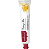 Slender white Red Seal Propolis toothpaste tube standing on a small red cap, with a red logo panel, black lettering and a golden honeycomb illustration near the top.