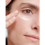 Close-up of a woman smoothing a white Dr Hauschka Regenerating Eye Cream streak beneath her eye with two fingertips.