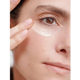 Close-up of a woman smoothing a white Dr Hauschka Regenerating Eye Cream streak beneath her eye with two fingertips.