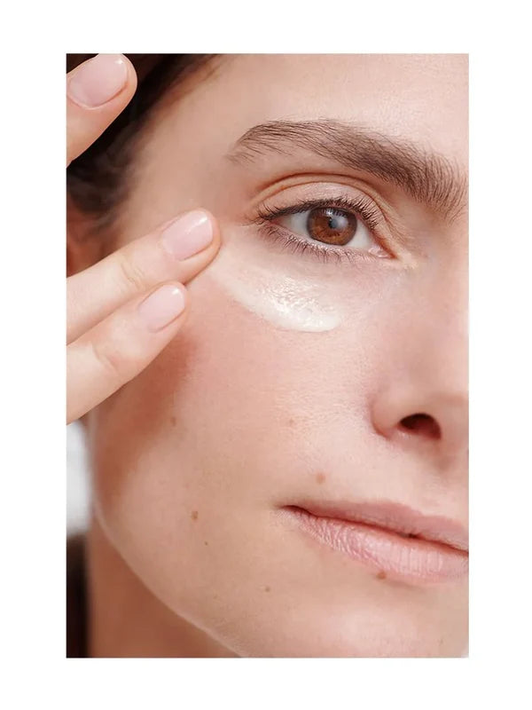 Close-up of a woman smoothing a white Dr Hauschka Regenerating Eye Cream streak beneath her eye with two fingertips.