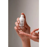 Hands holding an uncapped white Dr Hauschka Regenerating Eye Cream pump bottle, with a small white cream dab on an outstretched fingertip below it.