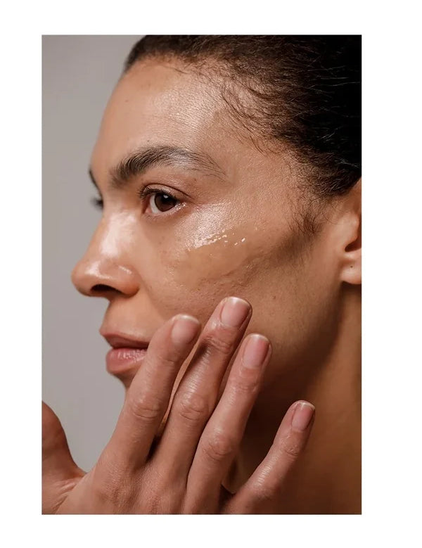 Close-up of a woman touching her cheek with her fingertips beside a glossy Dr Hauschka Regenerating Night Serum Intensive streak beneath her eye.
