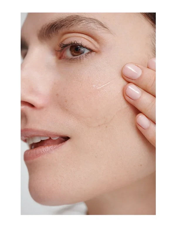 Close-up of a woman smoothing a thin, clear Dr Hauschka Regenerating Serum streak across her cheek with two fingertips.