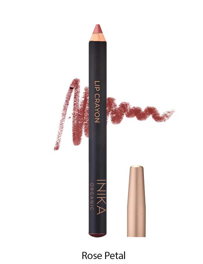 A rose-colored INIKA Organic Lip Crayon 6.7g with a swatch of the long-lasting lip liner shade scribbled behind it; the cap sits beside the crayon. Text below shows "Rose Petal.