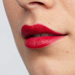 Close-up of a person's lips wearing vibrant red Antipodes Moisture Boost Natural Lipsticks 4g, with smooth skin visible around the mouth and nose. The words “Ruby Bay Rouge” appear at the bottom of the image.