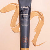 A gray tube labeled The Organic Skin Co Primp N' Prime Face Primer 60ml rests on a light surface, with beige primer cream swirled nearby. The tube has a wooden cap, gold accents, and promotes its radiant, vegan makeup primer formula.