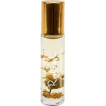 Slim clear Salt + Glow Restored roll-on perfume bottle with a shiny gold cap, pale golden liquid and dried golden-brown botanical pieces inside.