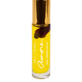 A clear glass bottle of Salt + Glow Elixir Roll on Perfume - Amore (Rose & Jasmine) 10ml, with yellow oil, a gold cap, and a dark flower petal inside. This handmade Australian floral perfume blends rose and jasmine notes.