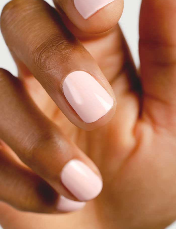A close-up of a hand with neatly manicured, short nails on medium brown skin, painted in Sienna Byron Bay Nail Polish - Serenity, a pastel pink champagne shade with a glossy, toxin-free finish for a fresh look.