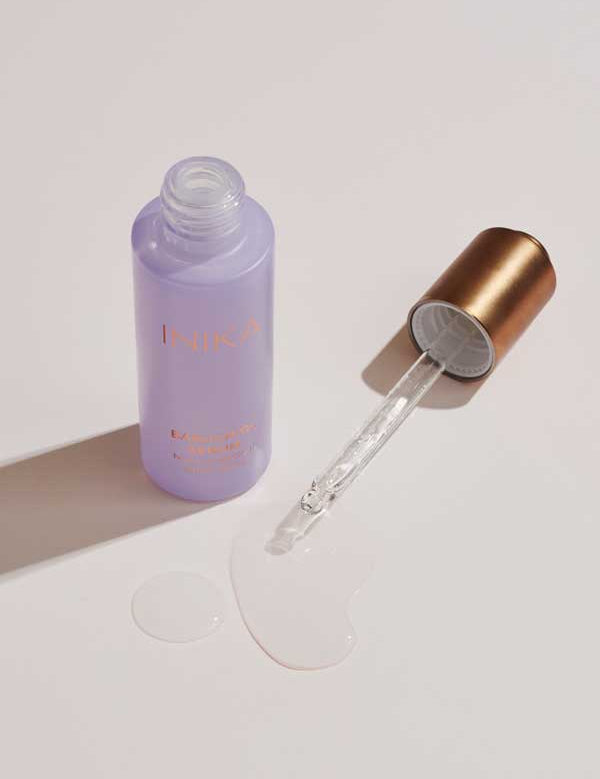 A lavender bottle labeled INIKA Organic Bakuchiol Serum Natural Retinol Alternative 30ml with a gold dropper cap lies open, clear liquid spilled nearby—a luxurious vegan retinol alternative for plant-based skincare lovers.