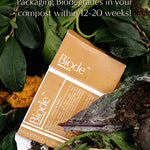 Mustard yellow Biode Into the Sunset shampoo packaging among leaves and compost. Overlaid text states that the packaging biodegrades in compost within 12–20 weeks.