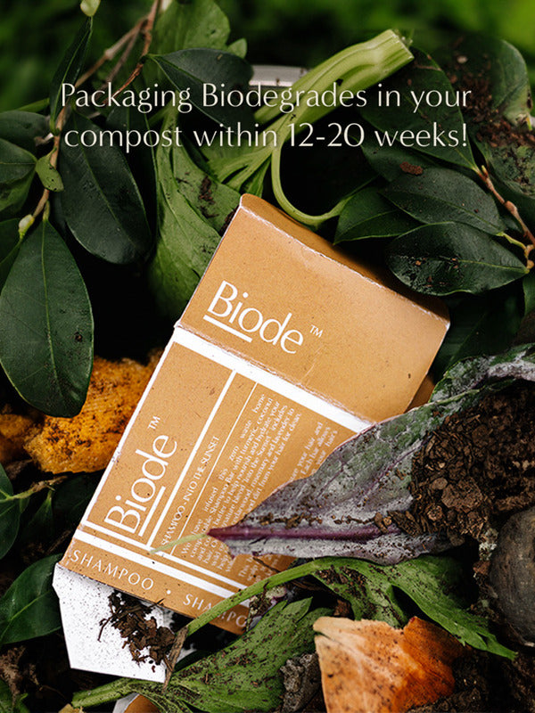 Mustard yellow Biode Into the Sunset shampoo packaging among leaves and compost. Overlaid text states that the packaging biodegrades in compost within 12–20 weeks.