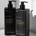 Black rectangular Vanessa Megan Yuzu & Rice Protein Conditioner and Bamboo & Rosemary Shampoo pump bottles stand together in sunlight, with water droplets on their surfaces.