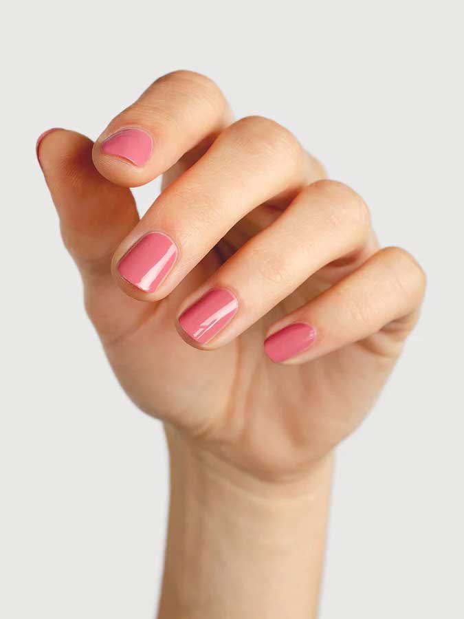 A close-up of a hand with neatly manicured nails painted in Sienna Byron Bay's Blossom, a glossy pink polish, set against a plain light gray background.