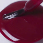 A close-up shows Sienna Byron Bay Nail Polish - Promise, a deep burgundy red, being brushed onto a white surface, forming a glossy puddle.