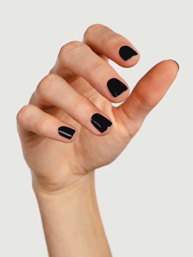 A hand with short, neatly manicured nails painted in Sienna Byron Bay's Onyx polish, set against a plain light background.