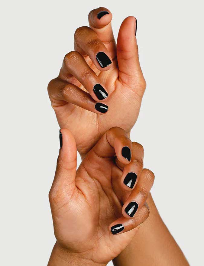 Two hands with dark skin, fingers gently intertwined, display short nails polished in glossy black using Sienna Byron Bay Nail Polish in Onyx by Sienna Byron Bay against a plain background.