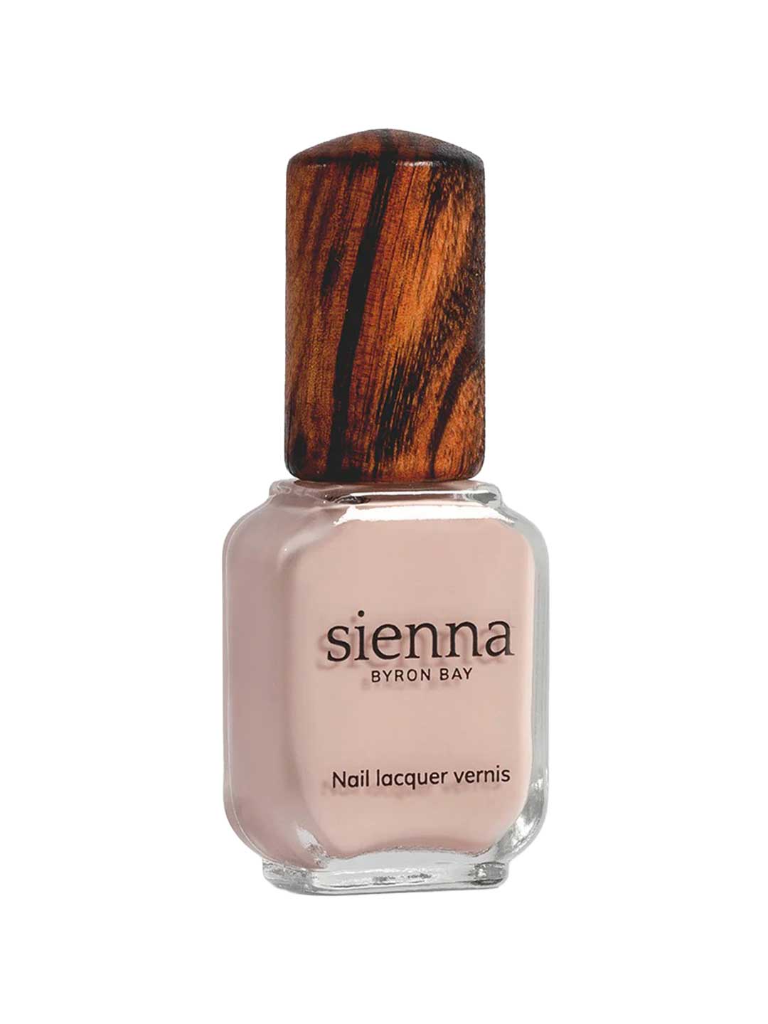 A bottle of Sienna Byron Bay Nail Polish - Posy in a light nude pink shade features a wooden-textured cap and label with the Sienna Byron Bay brand name and product details.