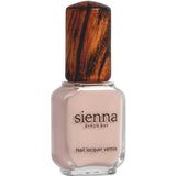 A bottle of Sienna Byron Bay Nail Polish - Posy in a light nude pink shade features a wooden-textured cap and label with the Sienna Byron Bay brand name and product details.
