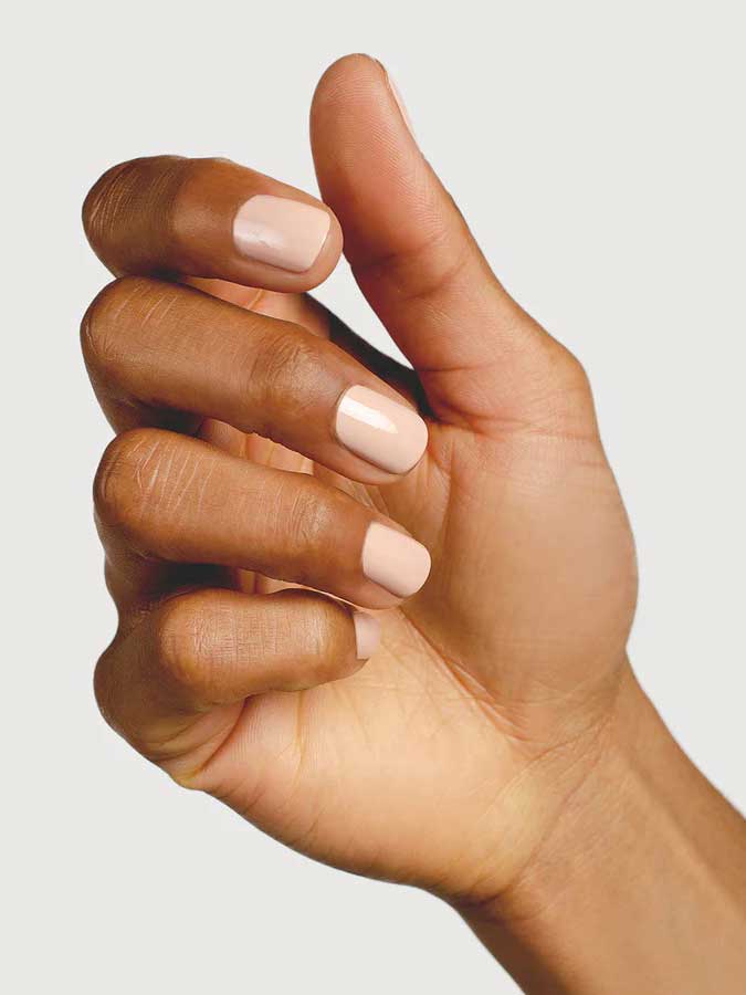A close-up of a hand with medium-brown skin and neatly manicured nails painted in Sienna Byron Bay Nail Polish - Posy, held against a plain light background.