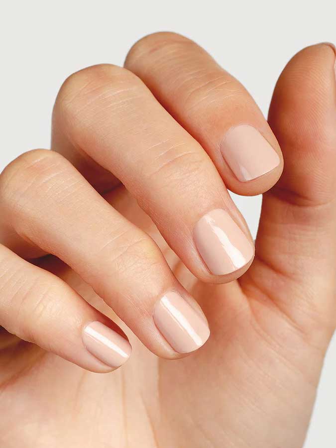 A close-up of a hand with neatly manicured nails painted in Sienna Byron Bay Nail Polish - Posy, a glossy pale nude shade, against a light background.