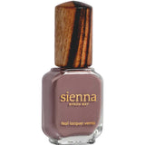 A rectangular glass bottle of Sienna Byron Bay Nurture nail polish, featuring a brownish-mauve shade, gold label with brand and product info, and a wooden cap.
