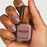 A hand with neatly manicured nails painted mauve holds a Sienna Byron Bay Nurture nail polish bottle, featuring its distinctive wooden cap.