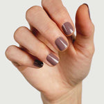 A hand with neatly manicured nails painted in Sienna Byron Bay Nurture, a glossy mauve-brown shade by Sienna Byron Bay, is held against a plain light background.