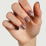 A hand with neatly manicured nails painted in Sienna Byron Bay Nurture, a glossy mauve-brown shade by Sienna Byron Bay, is held against a plain light background.